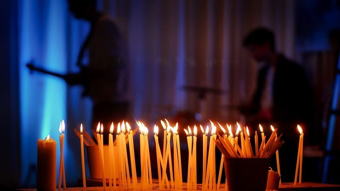 Viele brennende Kerzen in der Dunkelheit, zwei Personen im Hintergrund.