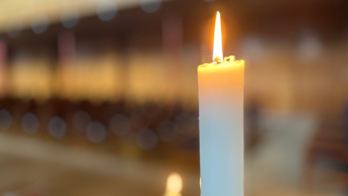 En lysende stearinlys i forgrunden, omgivet af udeblendete og skygger.