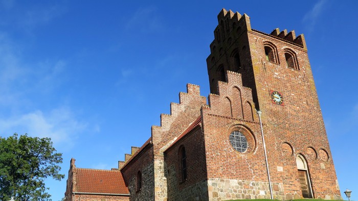 En middelalderkirke med tårn og gravsteder på en grøn bakke