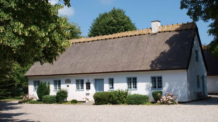 Hvidkalket landhus med tagstensovn og grønne planter foran