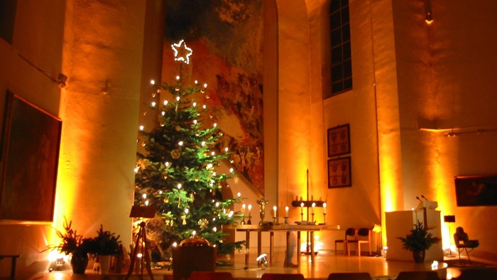 In der Kirche steht ein geschmückter Weihnachtsbaum vor einem großen Gemälde.