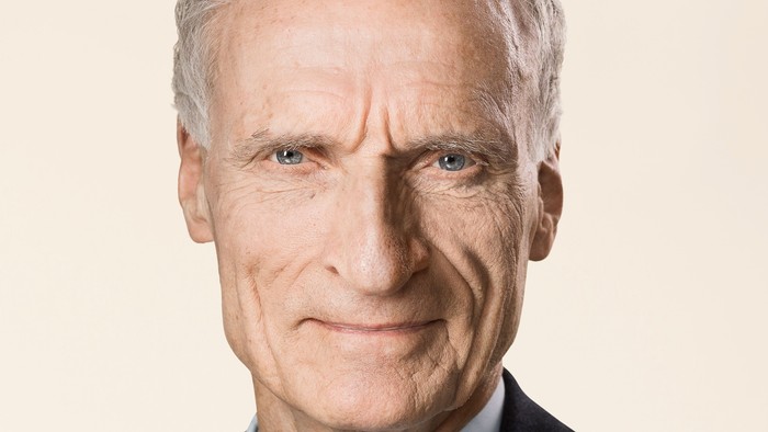 Gråhåret mand i jakkesæt og slips, der smiler.