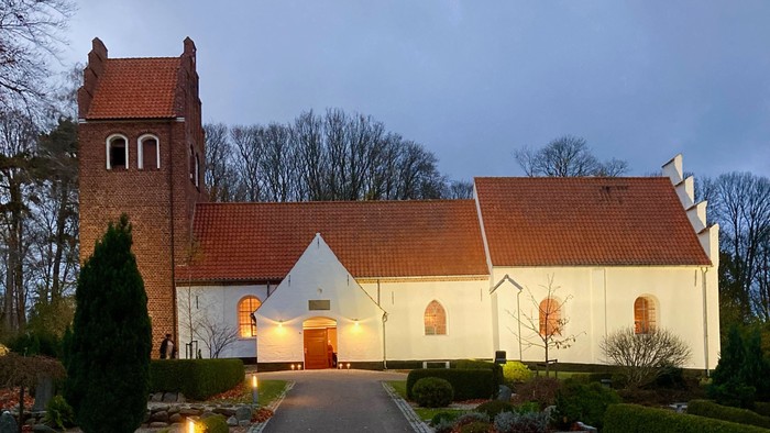 En lille kirke med røde tag og en smal asfaltvej der leder op til den