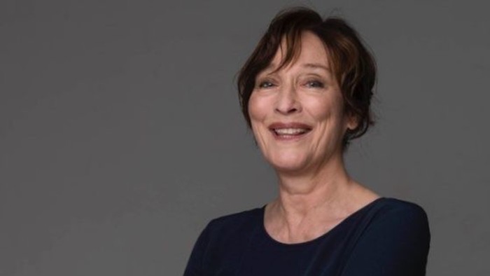 Kvinde med kort hår, der smiler, iført en mørk top på en neutral baggrund.