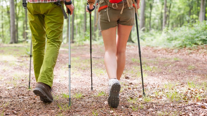 Zwei Personen wandern im Wald mit Trekkingstöcken.