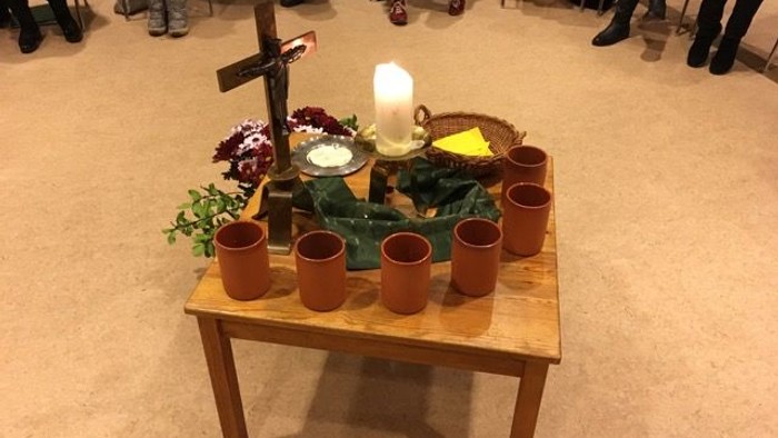 Ein Tisch mit Kerzen, Töpferarbeiten und Blumen in einem Raum mit Menschen.