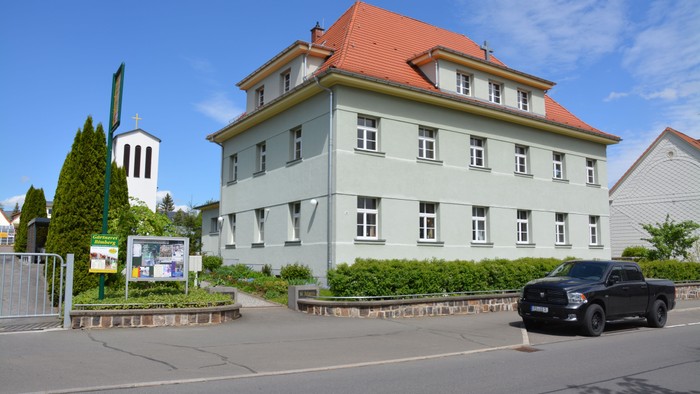 Ein großes, helles Gebäude mit rotem Dach und einem schwarzen Auto davor.