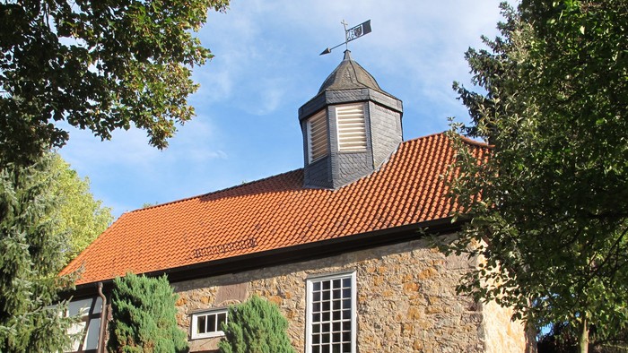 Steingebäude mit rotem Dach und Wetterhahn.