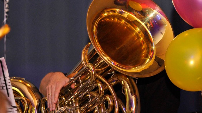 Eine Person spielt ein großes goldenes Tuba-Instrument, umgeben von bunten Ballons.