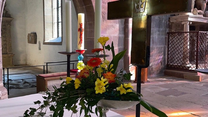 Eleganter Kirchenaltar, geschmückt mit lebendigen Blumen und einem großen Holzkreuz, in warmes Sonnenlicht getaucht.