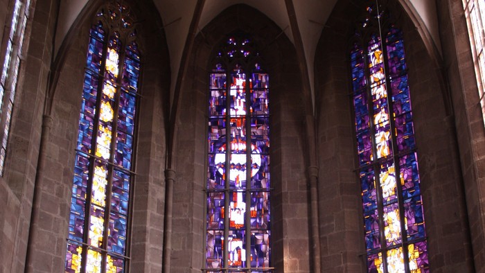 Drei hohe Buntglasfenster in einer Kirche.