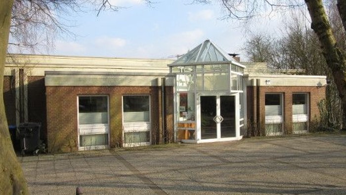 Das Bild zeigt ein modernes Gebäude mit Glasfront und Terrasse, umgeben von kahlen Bäumen und einem klaren Himmel.