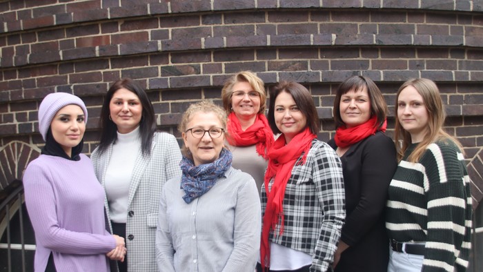 Eine Gruppe von sieben Frauen posiert vor einer Ziegelmauer