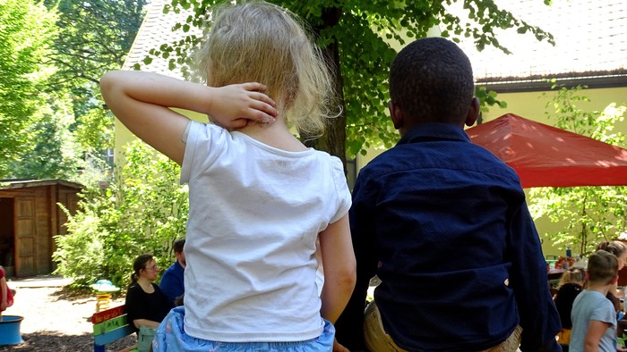 Zwei Kinder sitzen auf einer bunten Bank im Garten.