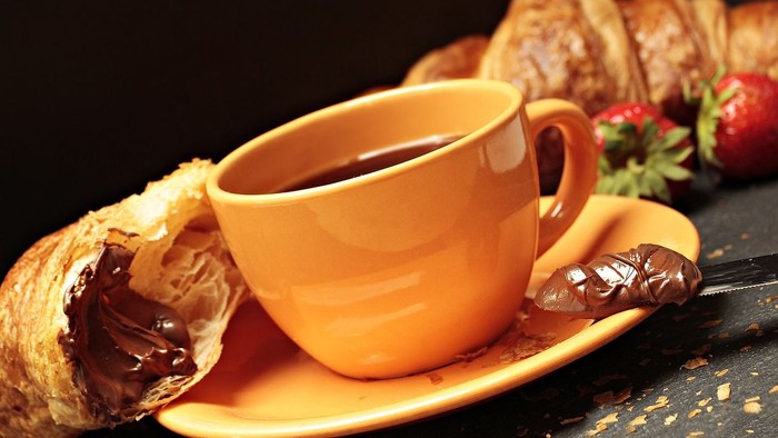 Ein orange Tasse mit Kaffee und ein Croissant mit Schokolade auf einem Teller
