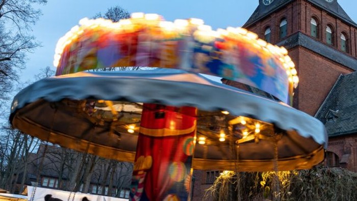 Ein Karussell dreht sich vor einem Ziegelgebäude mit Uhrturm bei Dämmerung.
