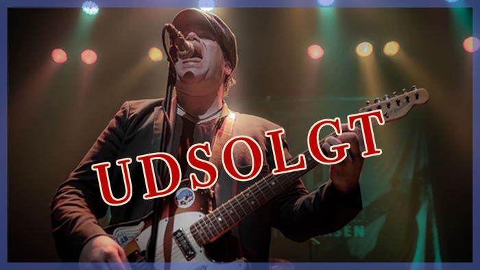 En musiker i kostume spiller guitar på scenen under farverigt lys med teksten 