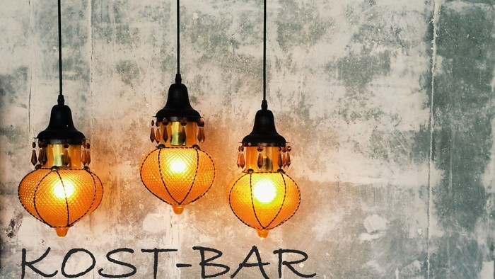 Drei hängende Lampen vor einem verwitterten Hintergrund mit der Aufschrift "KOST-BAR Messe am Samstagabend"