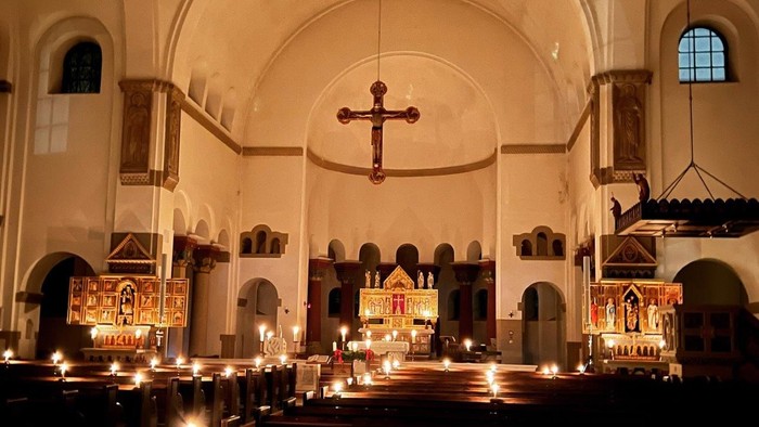 Innenraum einer Kirche mit brennenden Kerzen und Kreuz