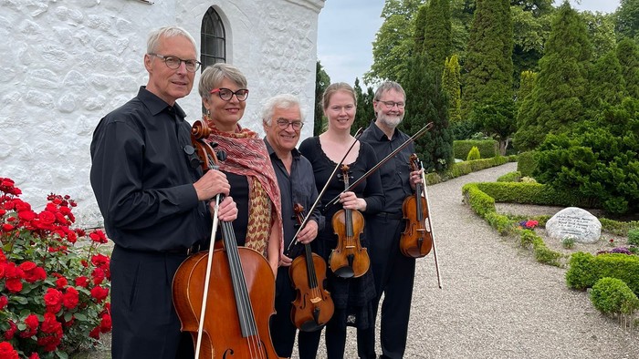Musikere poserer med instrumenter uden for en stenbygning.