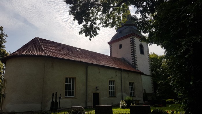 Kleine Kirche mit Turm und Uhr, umgeben von Bäumen