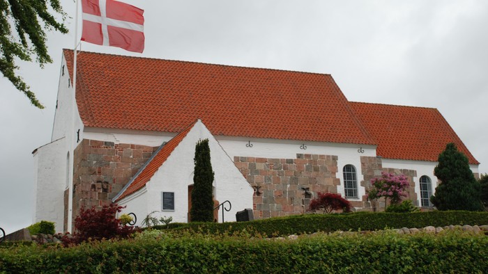 En hvid kirke med røde tag og en dansk flag på tårnet
