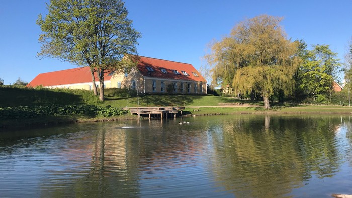 En rolig sø med et rødt taget hus og træer ved siden af