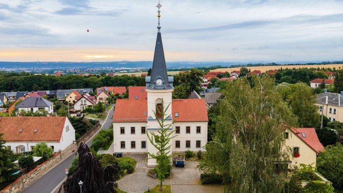 Kirchliche Anlage mit hohem Turm in kleinem Dorf, umgeben von Grünflächen und Häusern