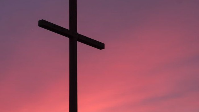 Ein Kreuz vor einem rosa-orangen Himmel