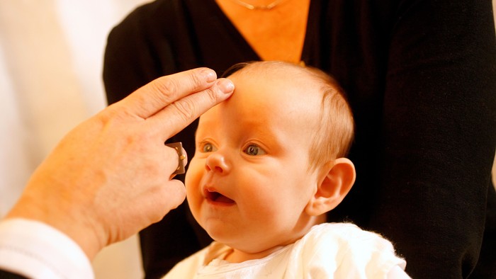 En person holder et barns hoved, mens et andet person taster barnets pande.