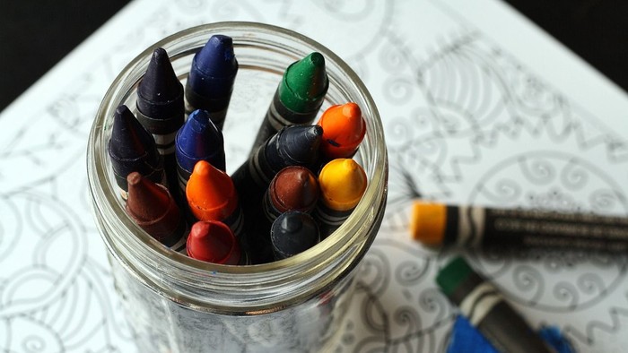 En glasflaske med farvede blyanter og en blyant på papiret