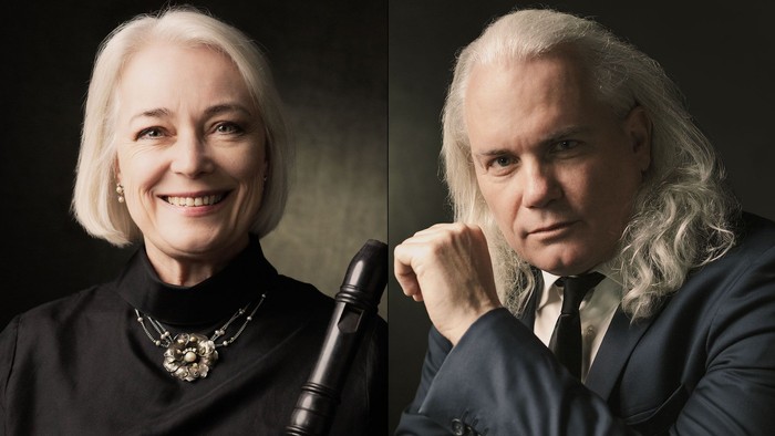 To personer, en smilende kvinde med blondt hår og en alvorlig mand med langt blondt hår, begge klædt formelt.