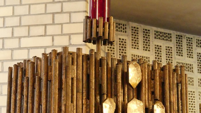 Ein hölzerner Kronleuchter mit goldenen Akzenten vor einer weißen Ziegelwand.