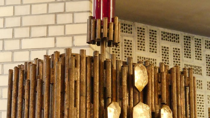 Ein hölzerner Kronleuchter mit goldenen Akzenten vor einer weißen Ziegelwand.