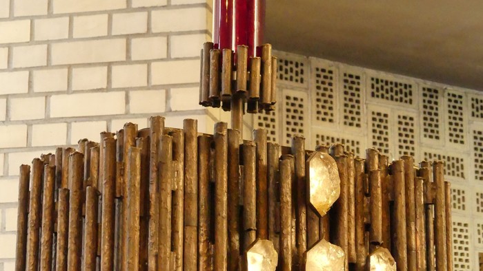 Ein hölzerner Kronleuchter mit goldenen Akzenten vor einer weißen Ziegelwand.