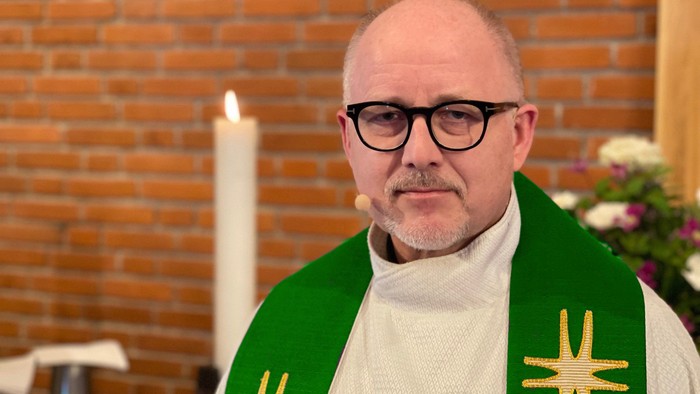 Mand i religiøs tøj foran murvæg og lysende ståske