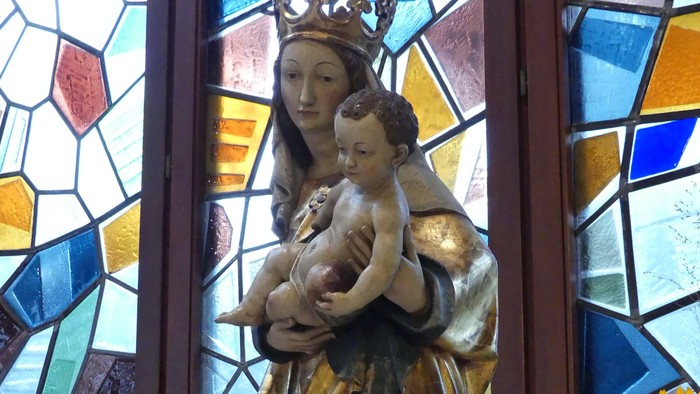 Heilige Muttergottes Statue vor buntem Kirchenfenster