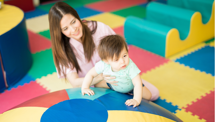 Mutter und Baby spielen auf bunten Schaumstoffmatten.