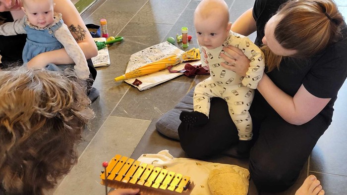 En gruppe børn og voksne sidder på gulv og spiller med legetøj.