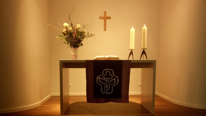 Ein Tisch mit Kerzen, Kreuz und Blumen in einem Raum