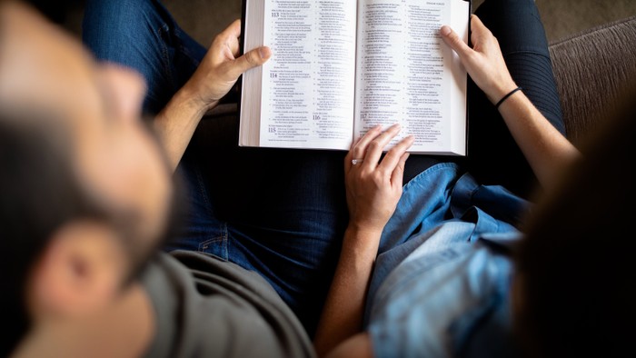 Two people reading a book together on a couch.