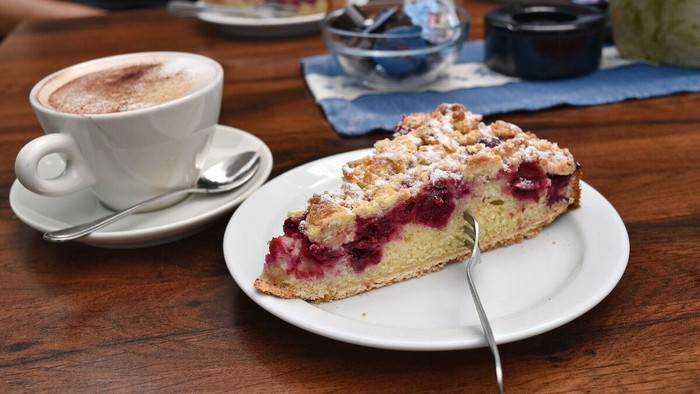 Ein Stück Kuchen mit Beeren und ein Kaffee auf einem Holztisch