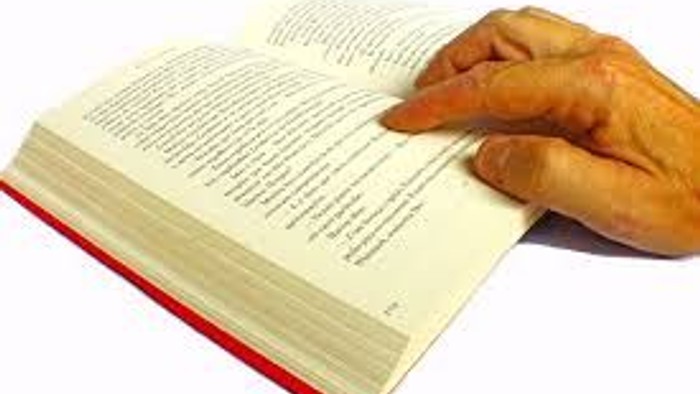 En hånd holder en bog med en brødstang på bladet.