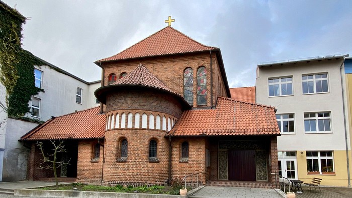 Das Bild zeigt eine rote Backsteinkirche mit spitzem Dach und einem kleinen Turm.