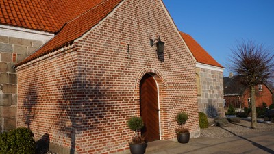 En lille murstenskirke med rødt tag og en dør med et tårn i oven.