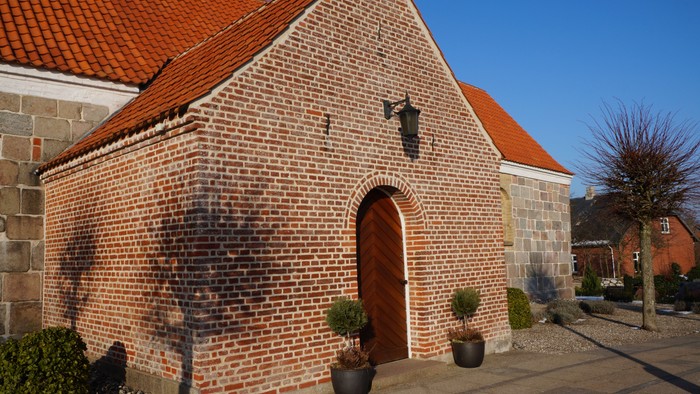 En lille murstenskirke med rødt tag og en dør med et tårn i oven.