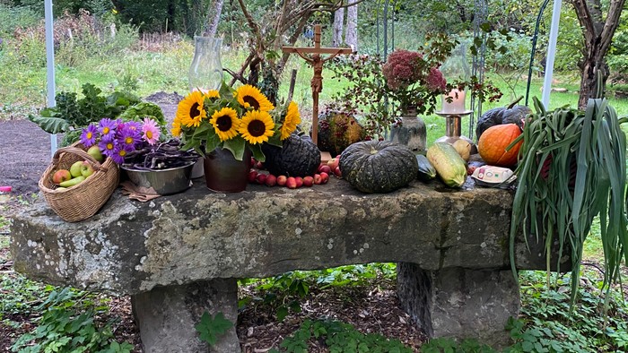 Ein steinerner Tisch im Garten mit Blumen, Kürbissen und Gemüse
