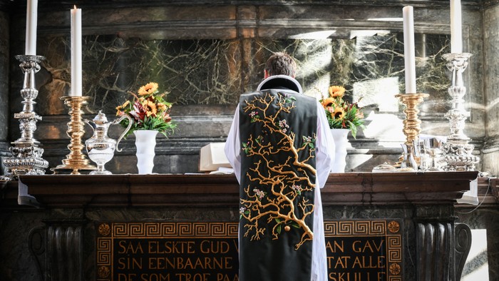 En præst står ved alteret med lysstaker og blomster.