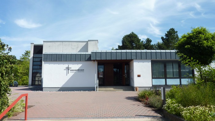Moderne Kirchengebäude mit einem Kreuzsymbol an der Fassade, errichtet auf einer mit Backsteinen gepflasterten Plattform.
