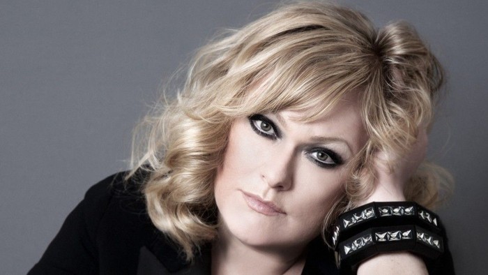 En kvinde med blondt hår og mørke klæder ser tænkende ud.